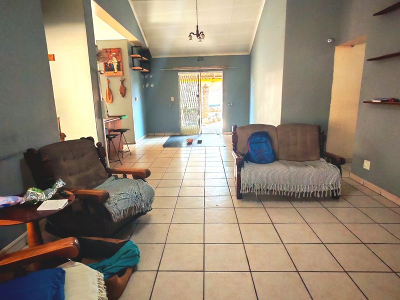 A spacious living area featuring ceramic floor tiles, a vaulted ceiling, and built-in wall shelving, leading to an exterior security gate.