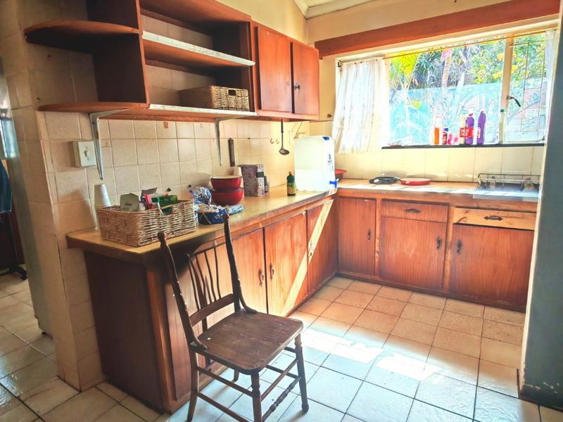 A dated kitchen featuring wooden cabinetry, tiled flooring, and a tiled backsplash, offering potential for a modern renovation.