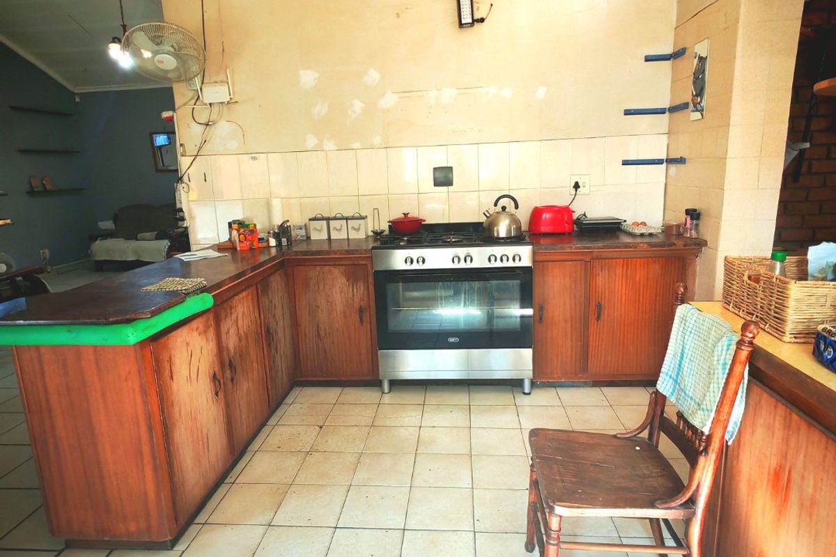 A dated kitchen featuring wooden cabinetry, a freestanding oven, and tiled flooring, requiring cosmetic updates to modernize the space.