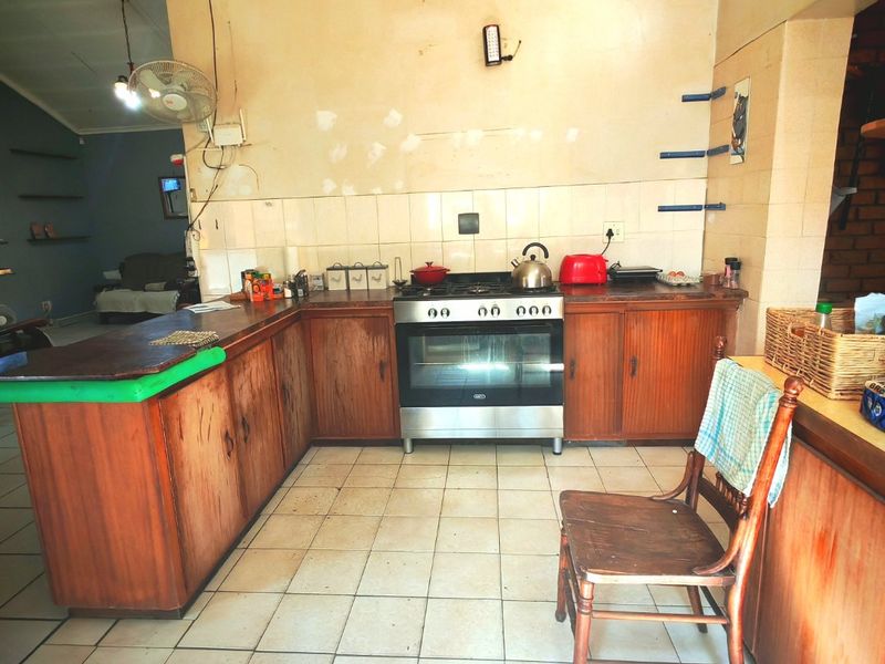 A dated kitchen featuring wooden cabinetry, a freestanding oven, and tiled flooring, requiring cosmetic updates to modernize the space.