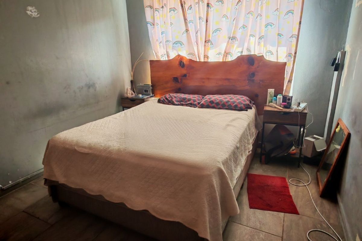 A bedroom featuring tiled flooring and a ventilation brick, currently showing signs of wear on the wall surfaces requiring maintenance or repainting.