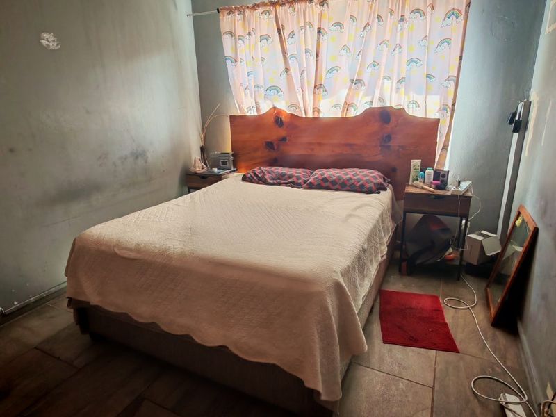 A bedroom featuring tiled flooring and a ventilation brick, currently showing signs of wear on the wall surfaces requiring maintenance or repainting.