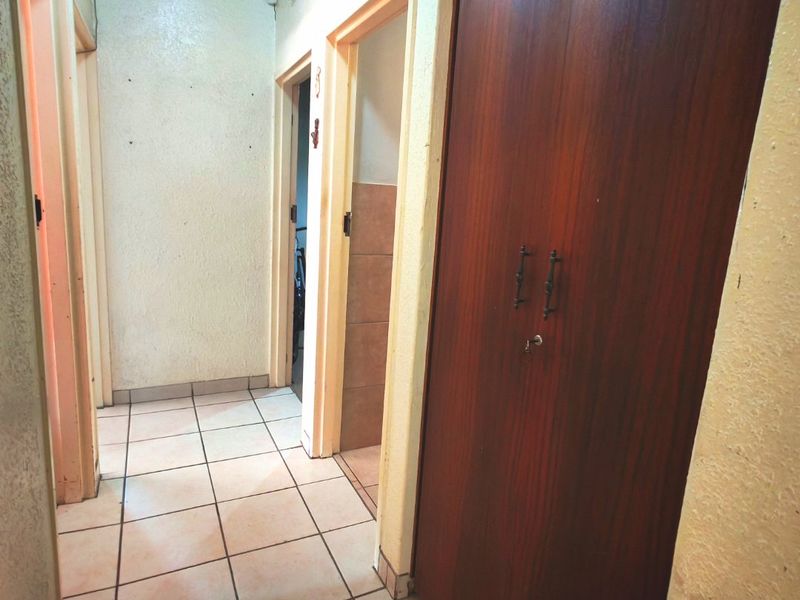 A functional hallway featuring tiled flooring and a large built-in wooden cupboard, providing access to multiple rooms within the home.