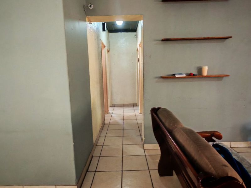 A living area featuring ceramic tile flooring and wall-mounted shelving, leading into a central hallway.