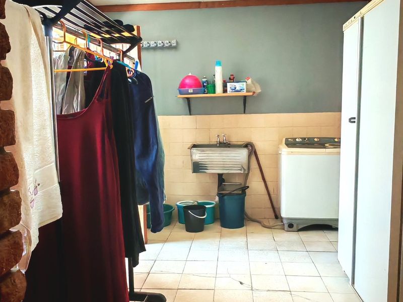A functional laundry area featuring a stainless steel utility sink, tiled splashback, and built-in storage cupboard with ceramic floor tiles.