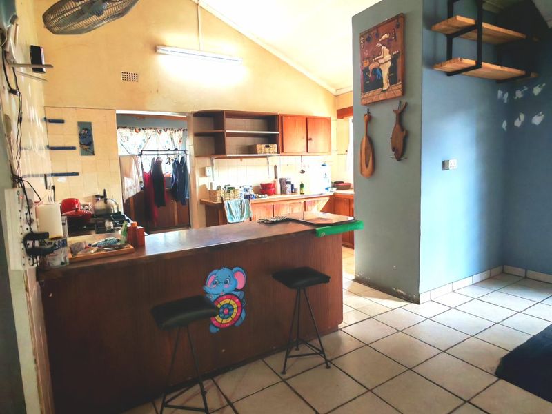 Open plan kitchen and living area featuring a breakfast bar, tiled flooring, and vaulted ceilings, offering potential for a modern renovation.