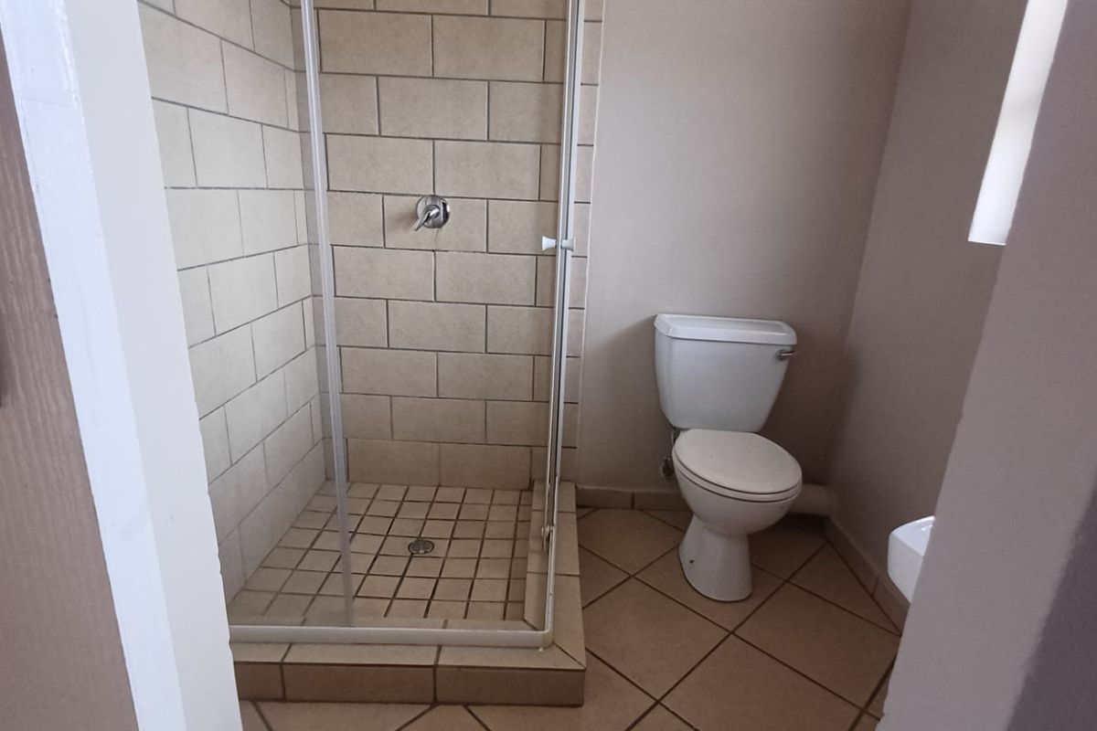 A functional bathroom featuring a tiled shower enclosure and a standard toilet, finished with neutral floor tiles.
