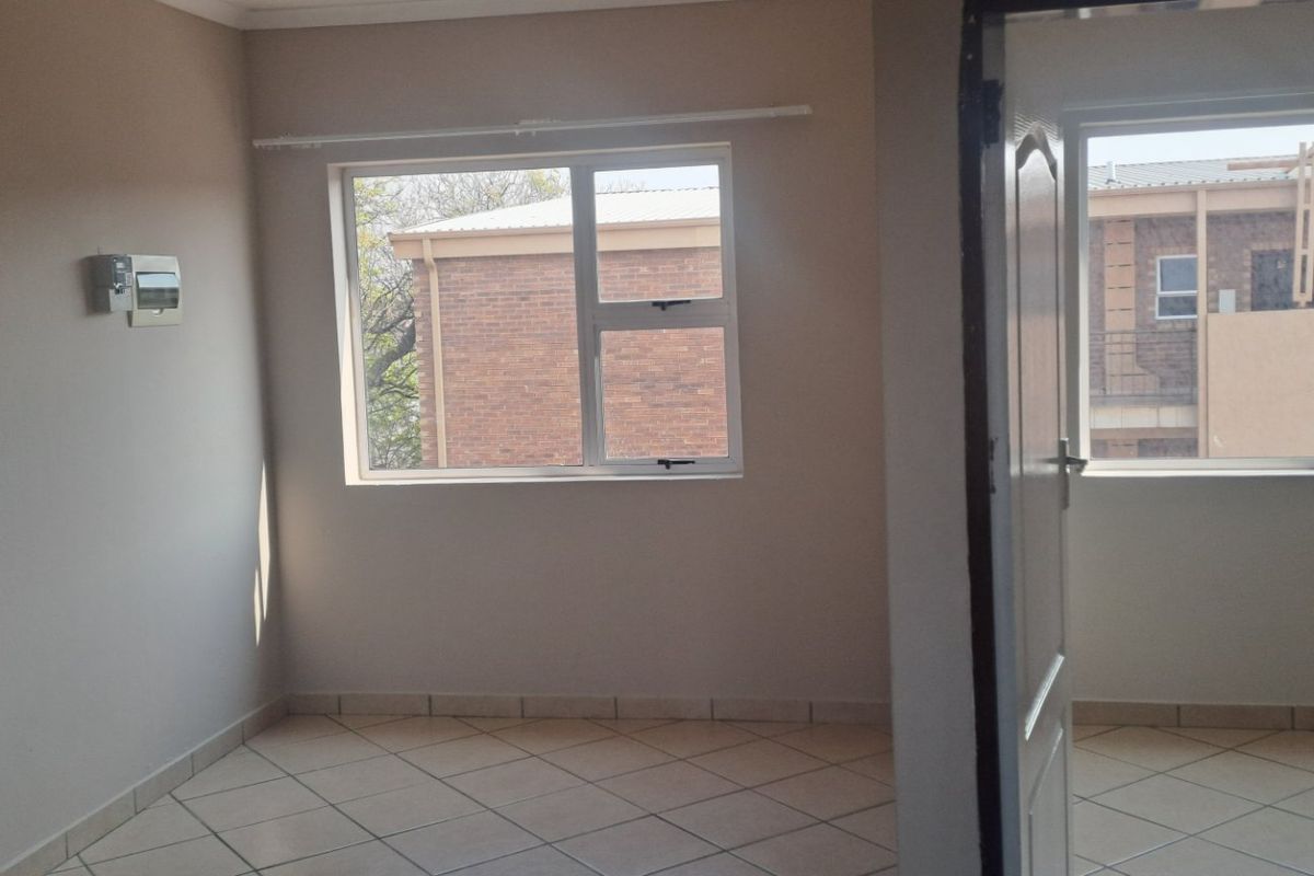 An empty living area featuring tiled flooring, neutral walls, and aluminium window frames, offering a clean and versatile space.