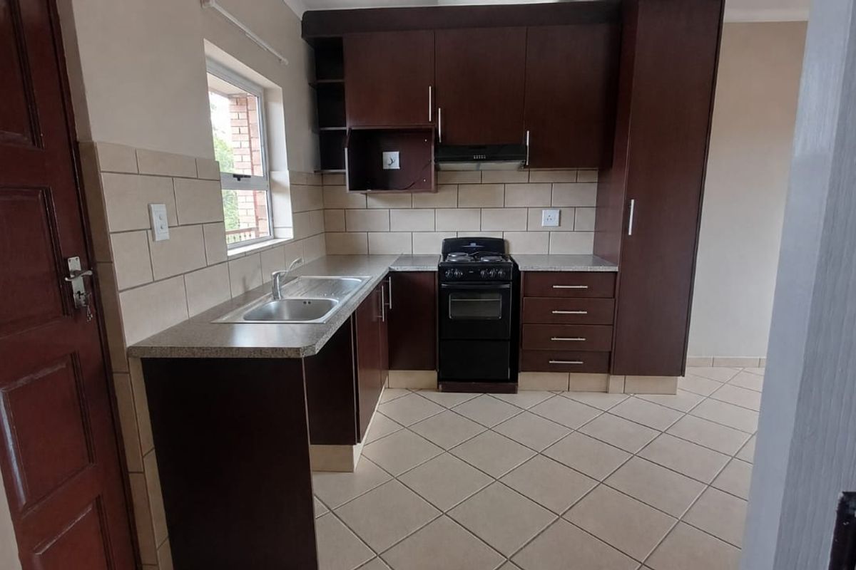 A clean, functional kitchen featuring dark wood cabinetry, laminate countertops, a tiled backsplash, and a freestanding stove with an extractor fan.