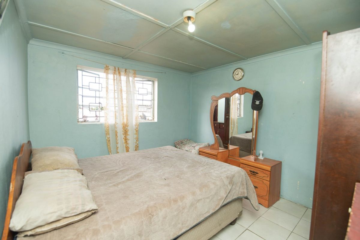 A bedroom featuring tiled flooring, security bars on the window, and a panelled ceiling. The room requires cosmetic updates to improve its overall condition.