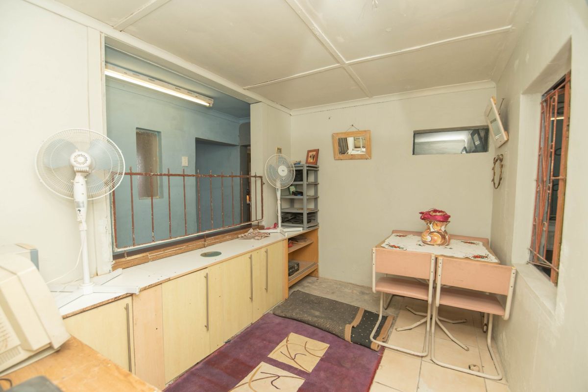 A functional kitchen area featuring built-in cabinetry, security bars on windows, and tiled flooring, offering potential for modernization and renovation.