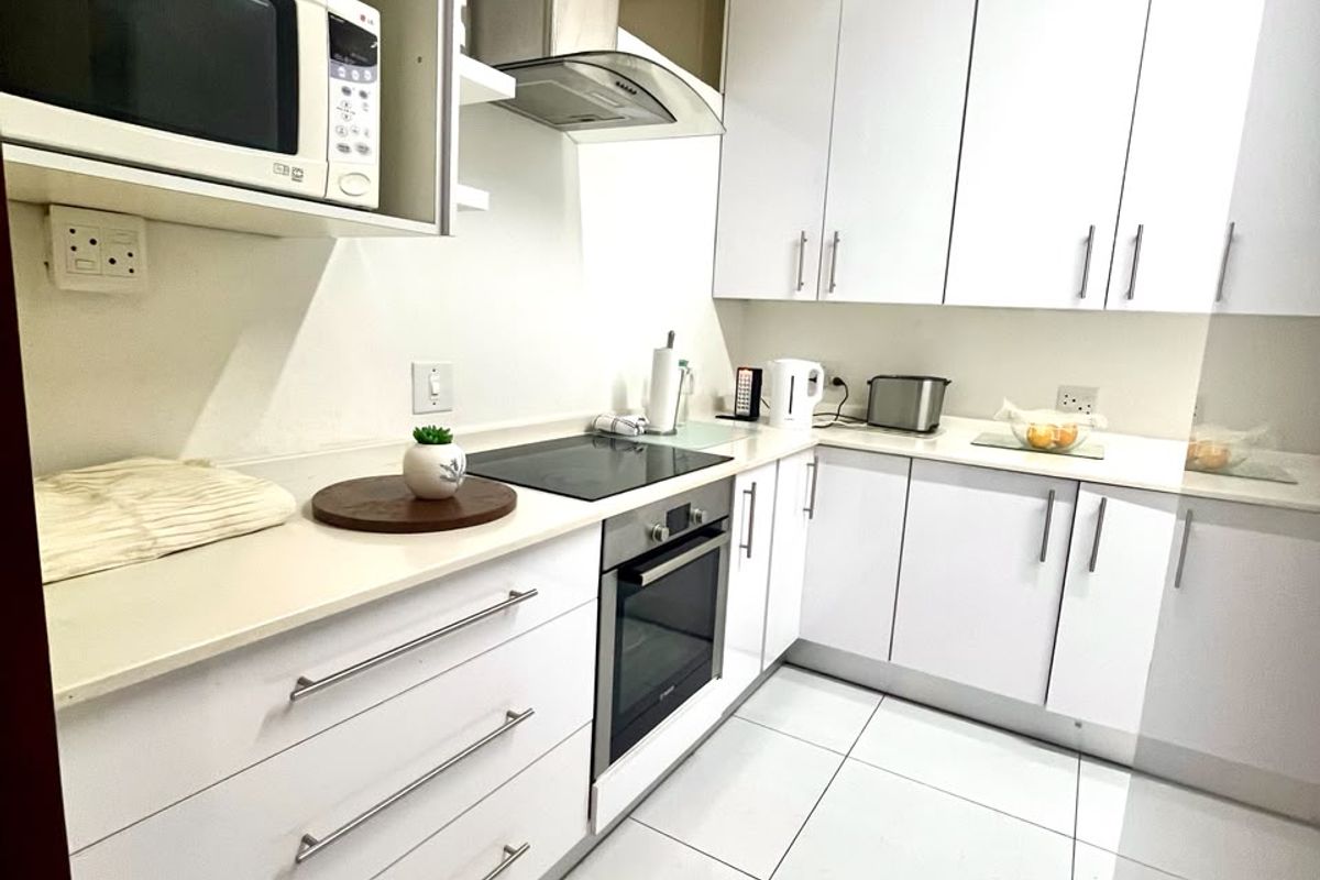 Modern kitchen featuring white high-gloss cabinetry, stone countertops, integrated appliances including an oven, hob, and extractor fan, complemented by clean tiled flooring.