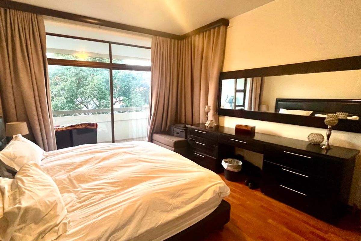 A bedroom featuring hardwood flooring, a built-in vanity with a large mirror, and sliding glass doors leading to a private balcony.