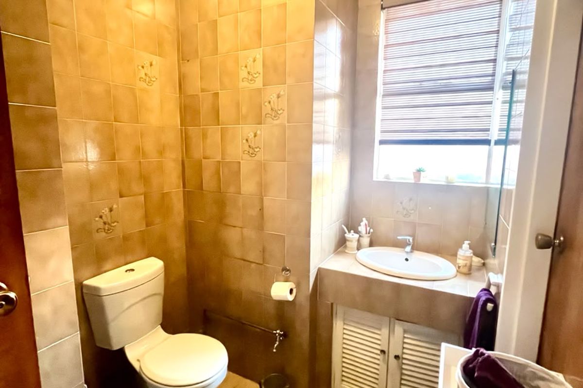 A compact bathroom featuring dated ceramic wall and floor tiles, a built-in vanity with a drop-in basin, and a standard toilet.