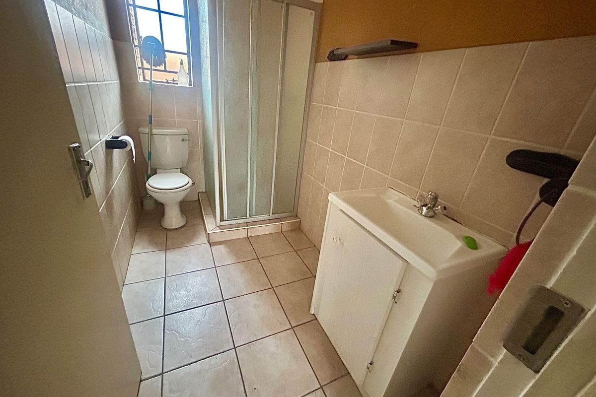 A functional bathroom featuring a shower enclosure, toilet, and vanity basin with tiled walls and flooring.