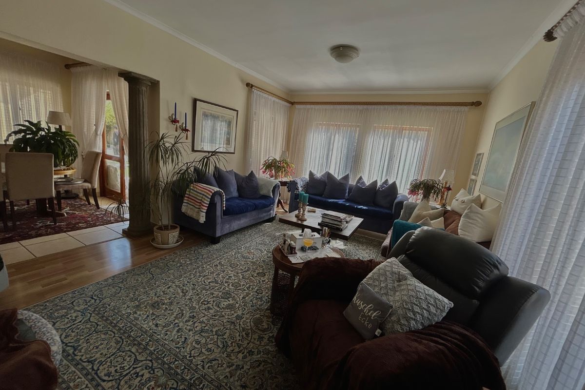 Spacious living room featuring hardwood flooring, a decorative column, and coved ceilings, with an open-plan flow into the adjacent dining area.