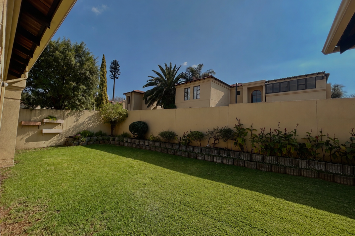 A well-maintained rear garden featuring a manicured lawn, perimeter boundary wall, and low-level retaining wall with established garden beds.