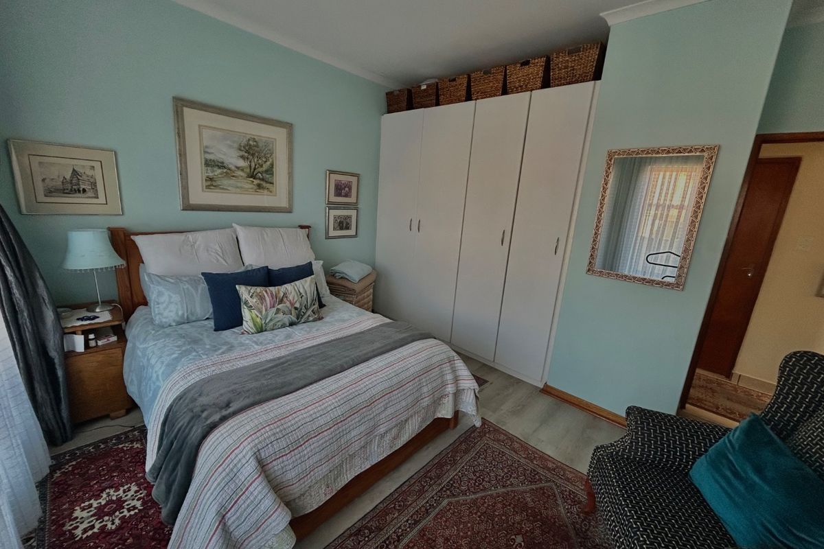 A well-maintained bedroom featuring built-in cupboards, light-toned laminate flooring, and soft blue wall finishes.