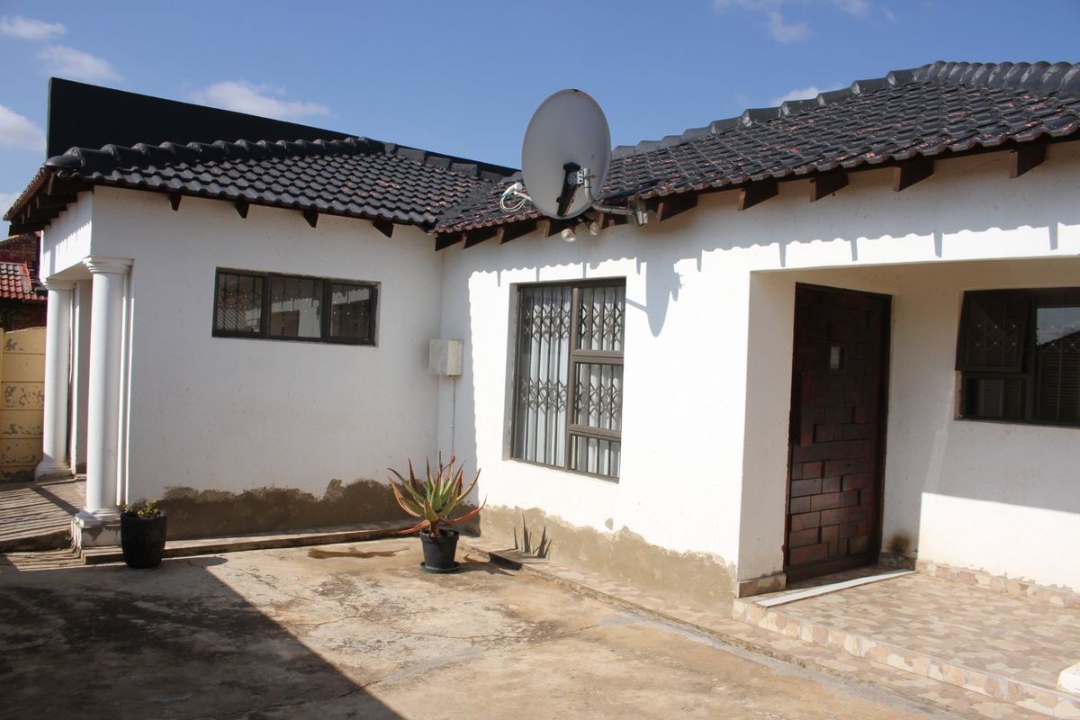 Rear exterior view of the property featuring a tiled roof, security gates, and a concrete patio area showing signs of wear and maintenance needs.