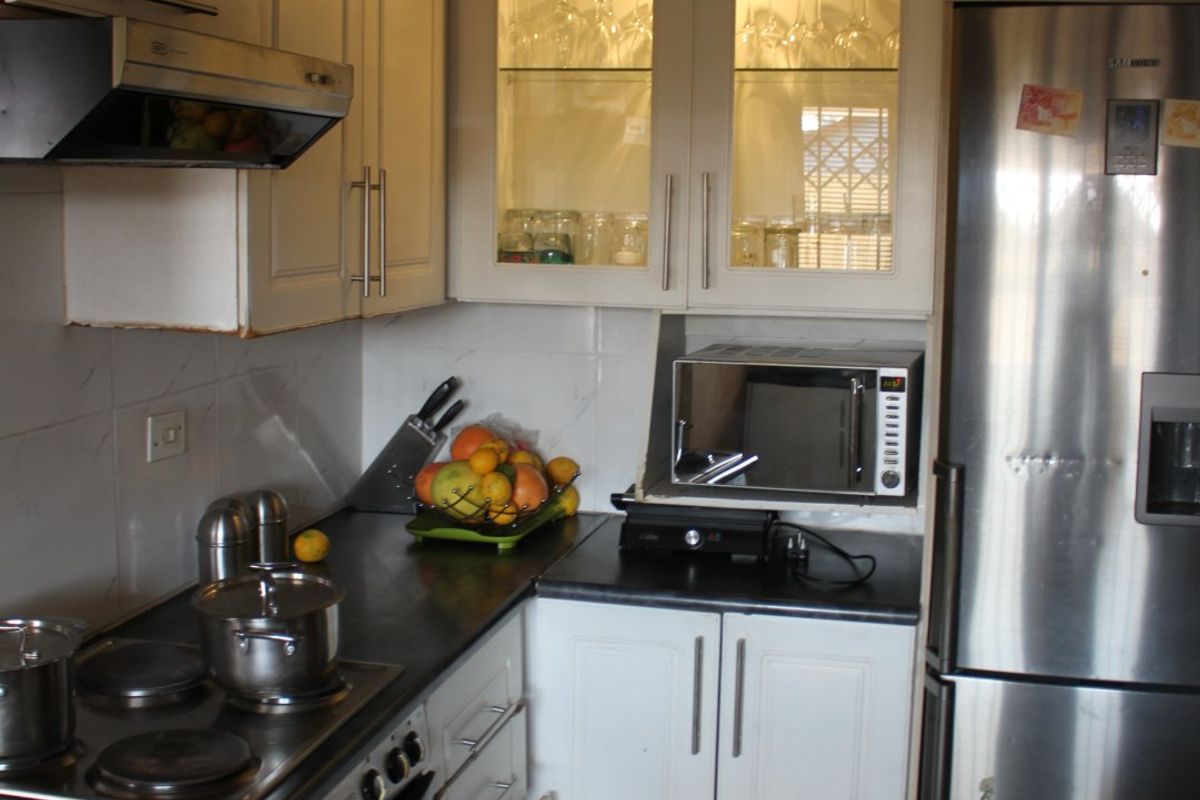 A functional kitchen featuring white cabinetry, an electric stove with extractor fan, built-in microwave, and tiled flooring, offering a practical layout for daily cooking.