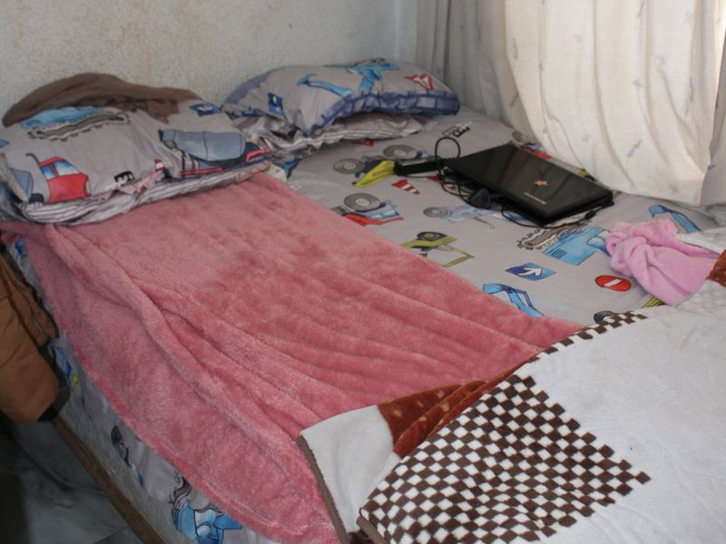 A compact bedroom featuring tiled flooring and visible wall surface deterioration, requiring maintenance and cosmetic updates.