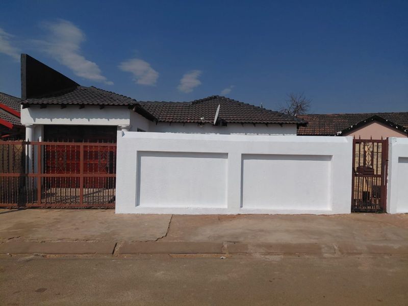 Front view of a residential property featuring a white perimeter wall, metal driveway gate, and tiled roof structure.