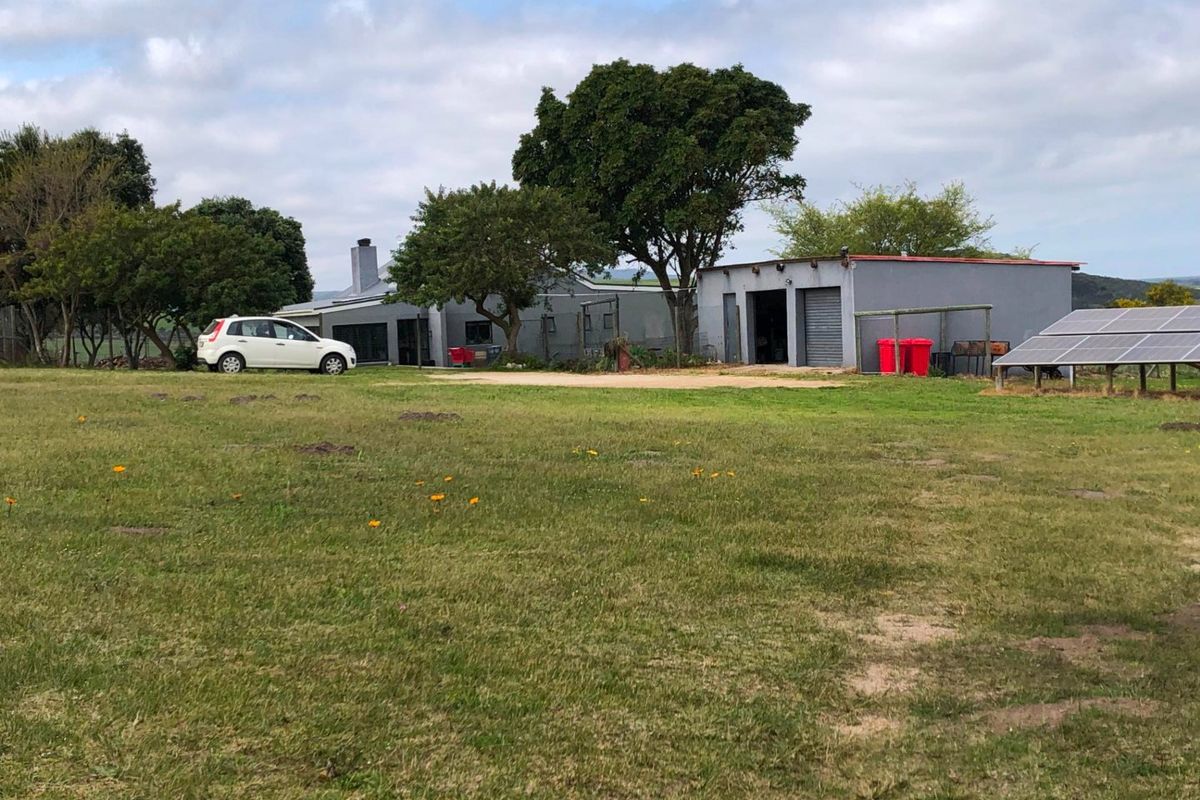 A view of the rear of the farm property featuring a garage, solar panel installation, and a large open grass area.
