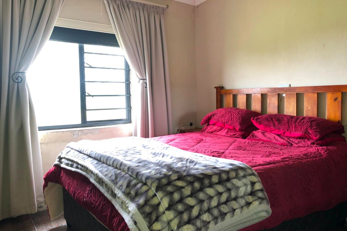 A bedroom featuring tiled flooring, a timber ceiling, and an aluminium window frame with visible plaster damage below the window sill.