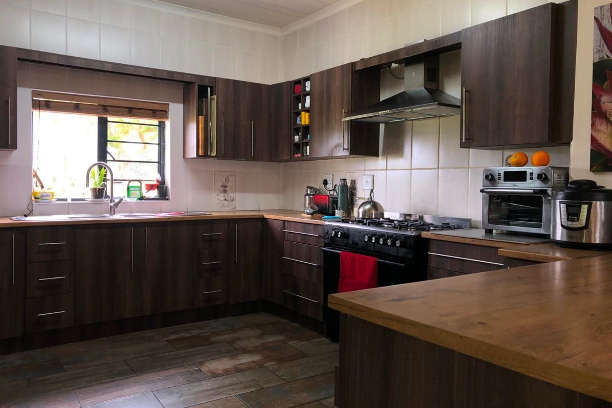 A functional kitchen featuring dark wood cabinetry, laminate countertops, a gas stove with extractor fan, and tiled flooring with a neutral backsplash.