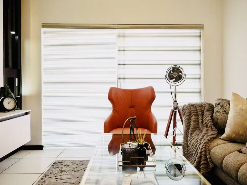 A well-lit living room featuring tiled flooring, built-in cabinetry, and large sliding glass doors fitted with modern zebra blinds.