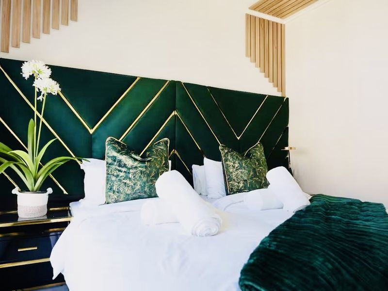 A well-appointed bedroom featuring a custom green and gold upholstered headboard with decorative timber wall paneling.