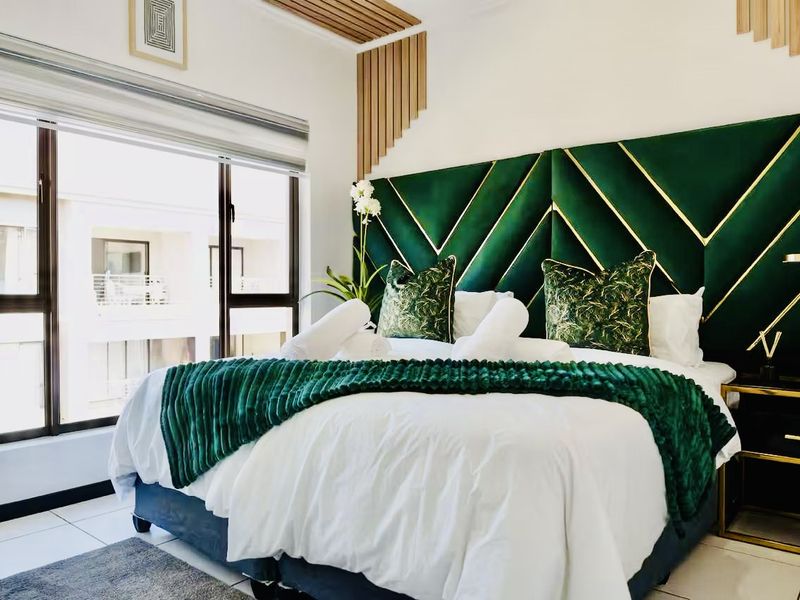 A well-appointed bedroom featuring a large window, modern slatted wood ceiling accents, and a striking custom upholstered headboard.