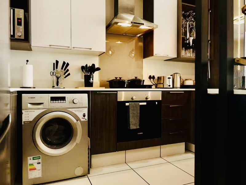 Modern kitchen featuring sleek laminate cabinetry, built-in oven, extractor fan, integrated microwave, and a washing machine, complemented by tiled flooring and a glass splashback.