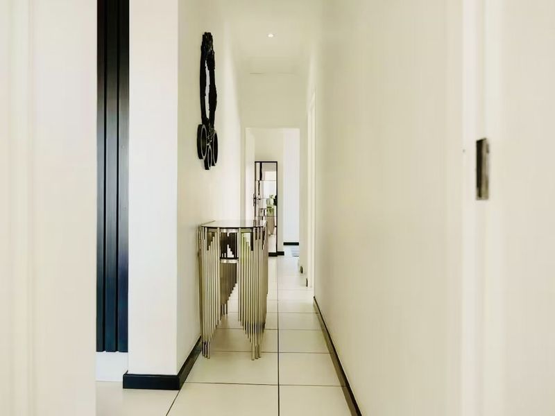 A bright and modern hallway featuring clean white walls, tiled flooring, and recessed downlighting, creating a seamless transition between living spaces.