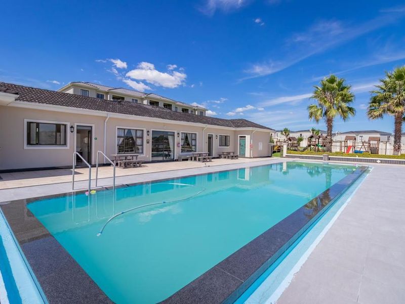 A well-maintained outdoor swimming pool area featuring a tiled deck, granite coping, and clear water, set within a clean apartment complex environment.