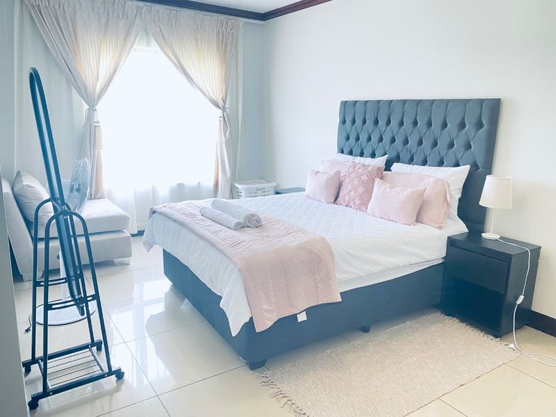 A bright and well-maintained bedroom featuring polished tiled flooring and large windows with installed curtain rails.