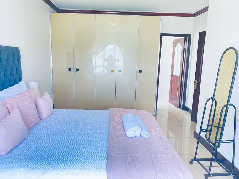A well-maintained bedroom featuring glossy built-in wardrobes, tiled flooring, and crown molding, with an adjoining doorway leading to an ensuite bathroom.