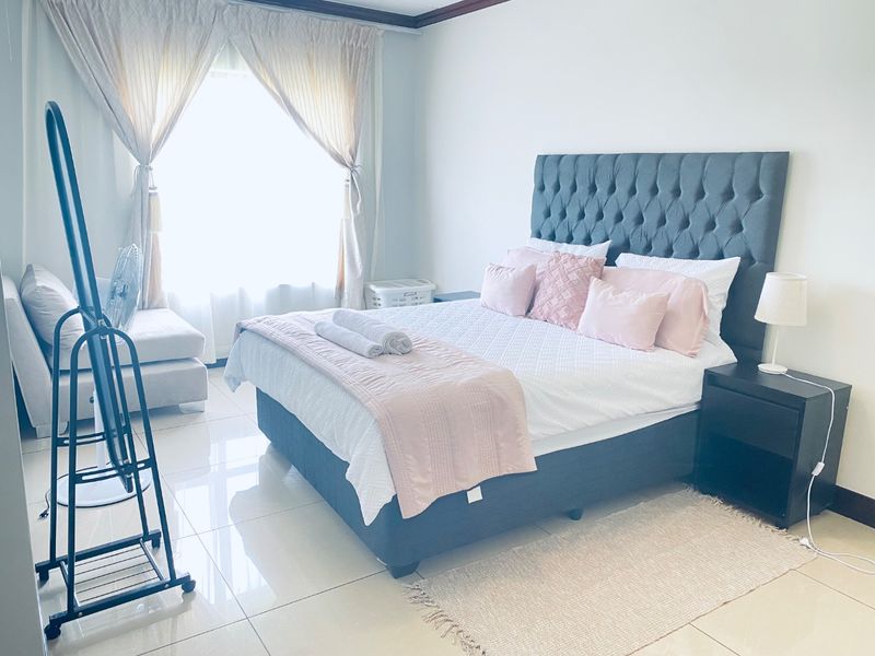 A bright and well-maintained bedroom featuring tiled flooring and large windows with curtain rails, offering a clean and comfortable living space.