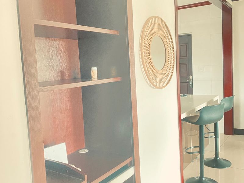 Open plan living area featuring a built-in wooden shelving unit and a breakfast bar with tiled flooring throughout.