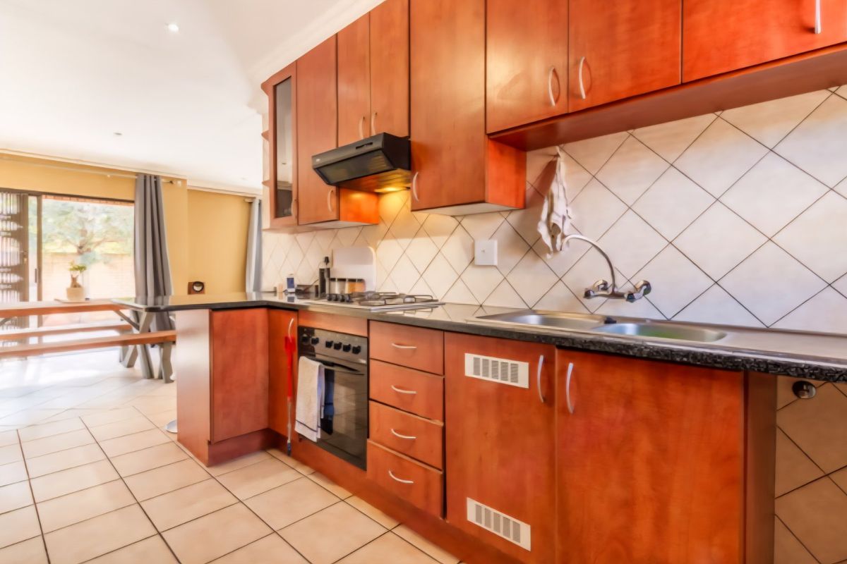 A functional kitchen featuring warm-toned wooden cabinetry, granite countertops, a built-in oven with gas hob, and a tiled backsplash.