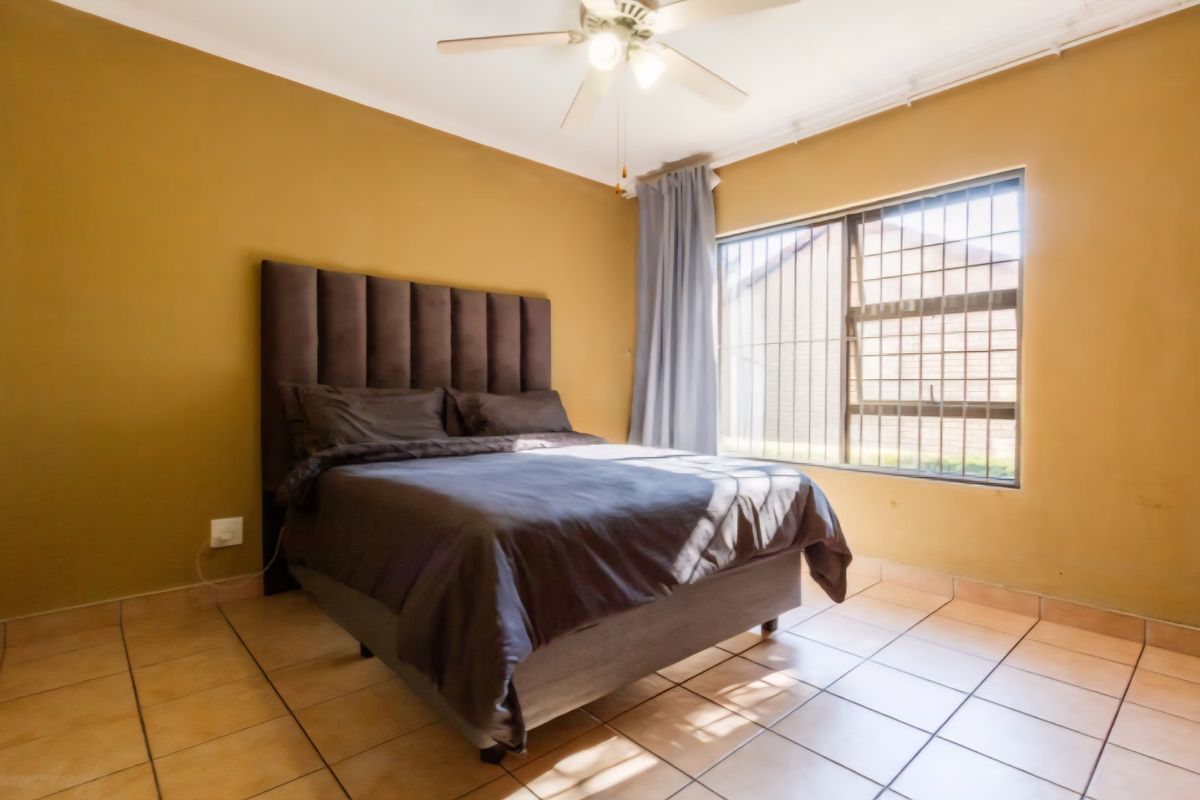 A bedroom featuring tiled flooring, a ceiling fan, and a window fitted with security bars.