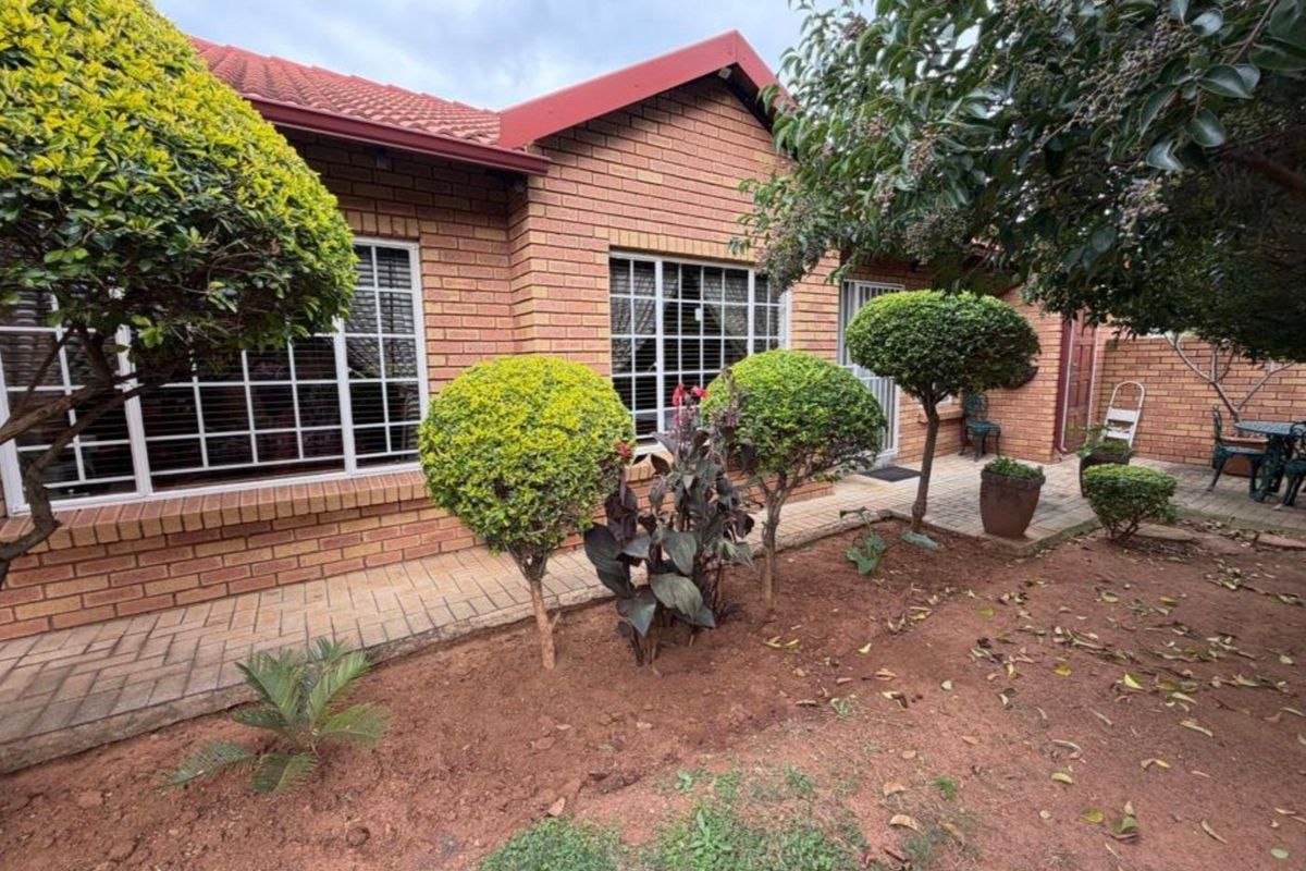 A well-maintained townhouse rear exterior featuring face brick walls, a tiled roof, and a paved walkway leading to the garden area.