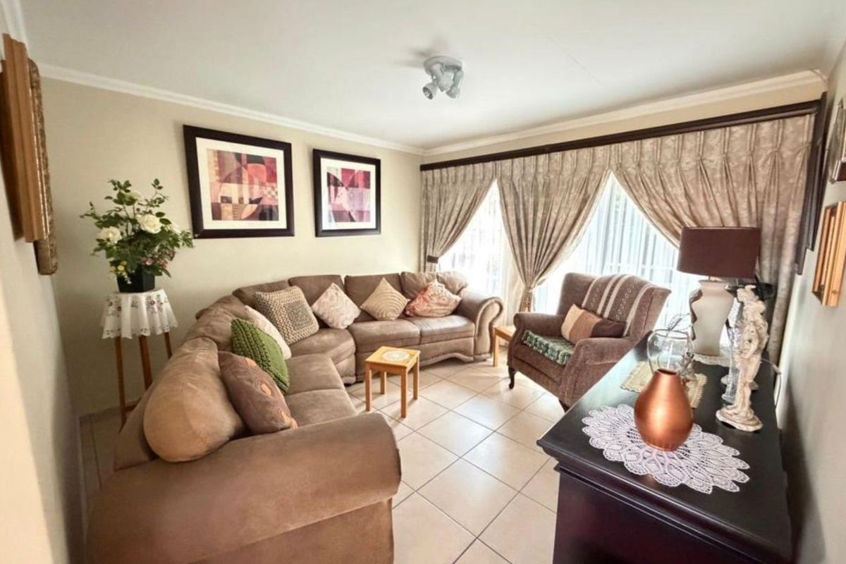 A comfortable living room featuring neutral ceramic floor tiles and large windows dressed with classic curtains, providing a functional and well-lit space.