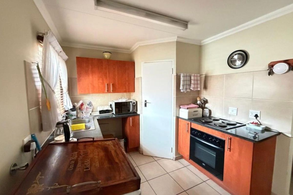 Functional kitchen featuring wooden cabinetry, granite countertops, built-in oven and hob, double sink, and tiled flooring.