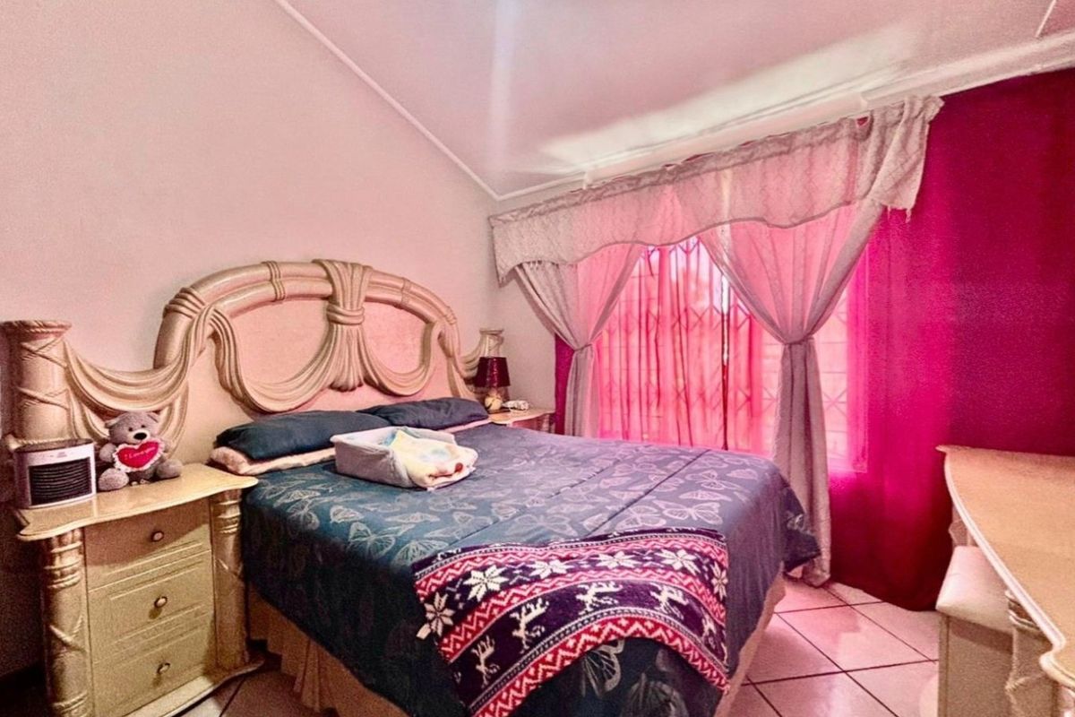 A bedroom featuring tiled flooring, a vaulted ceiling, and a window fitted with a security gate.