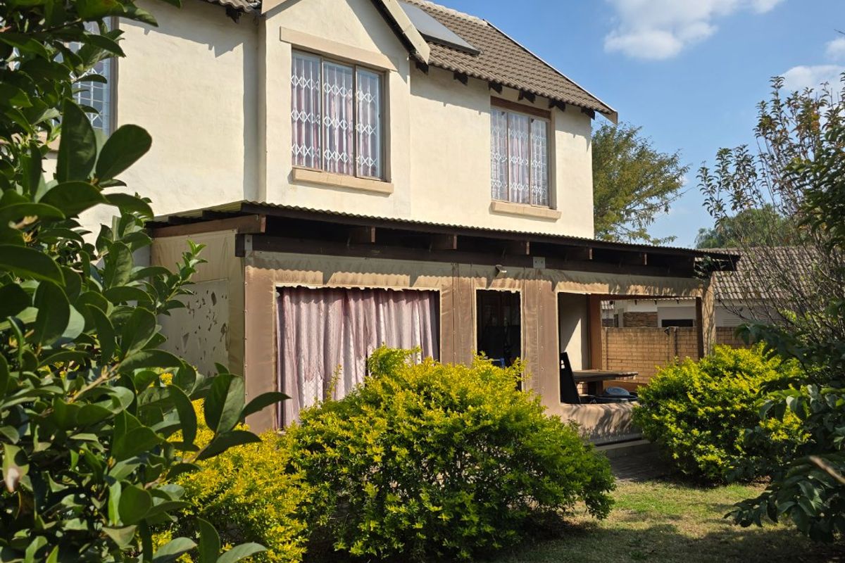 Rear view of a two-story townhouse featuring a covered patio area, established garden, and solar water heating system on the tiled roof.