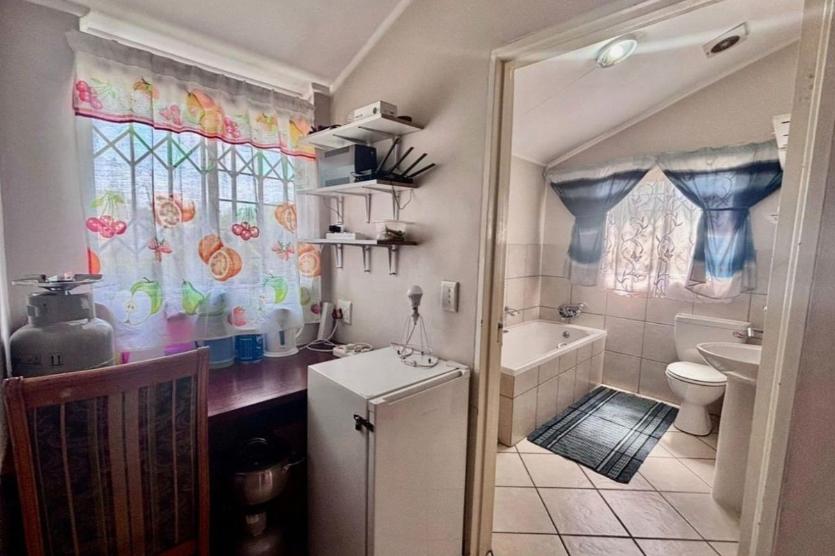A functional bathroom featuring a built-in bathtub, pedestal sink, and ceramic floor tiling, adjacent to a small utility or prep area.