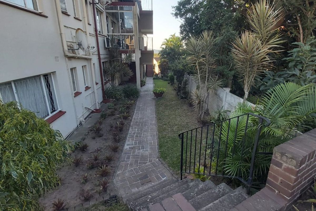 Rear view of the apartment building featuring a brick paved walkway, landscaped garden area, and concrete staircase access.