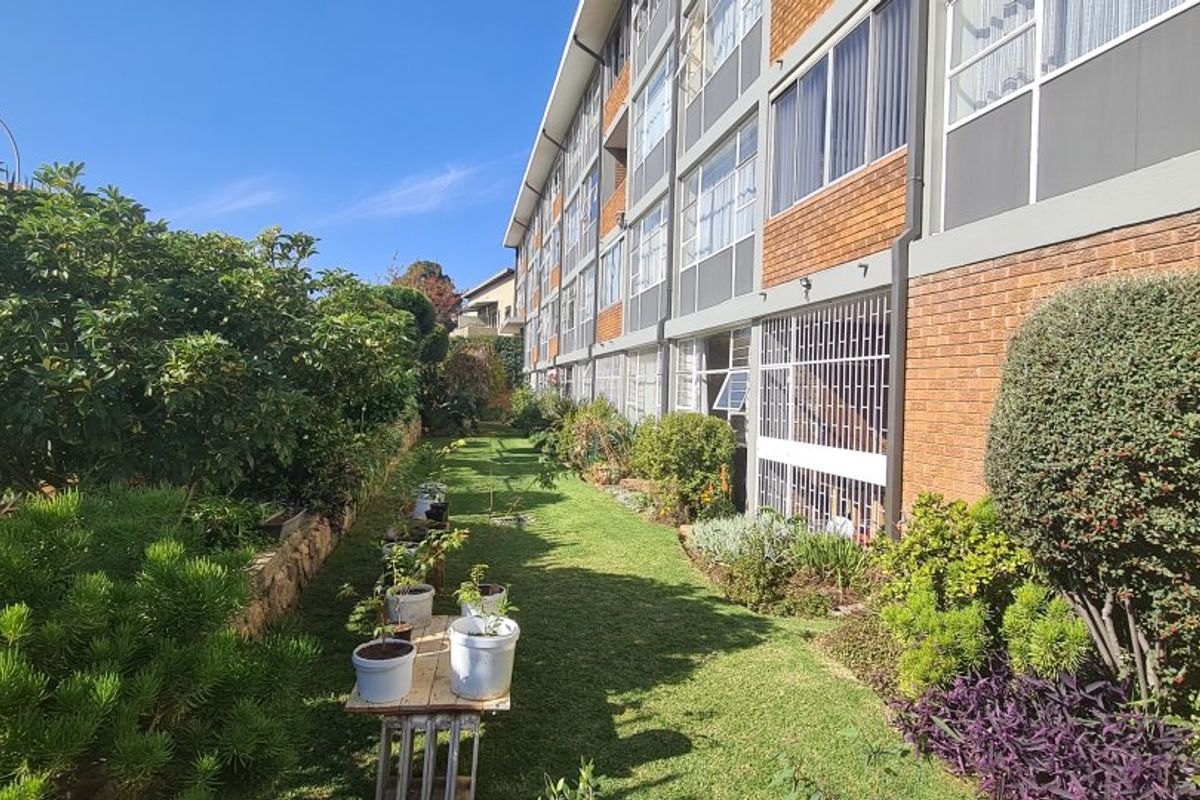 Rear view of the apartment building showing the brick facade, security bars on ground floor windows, and a landscaped garden area.