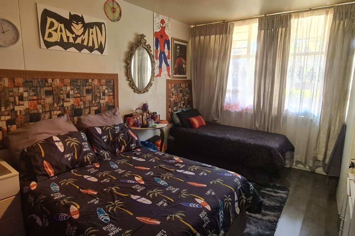 A bedroom featuring laminate flooring and a built-in headboard, with large windows allowing natural light through the curtains.